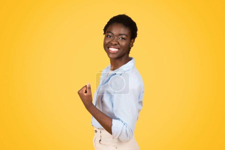 A black woman student, exuding triumph and joy, raises her fist in a victorious gesture over a bright yellow background, symbolizing her success and determination in her academic endeavors