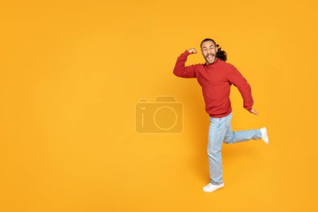 Photo for Excited young man clenching fist and running over yellow orange studio background, have great news. Happy guy hurry up, full length shot with copy space for advertisement - Royalty Free Image