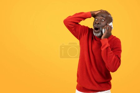 Téléchargez les photos : Choqué homme noir senior dans un pull rouge tenant un téléphone à son oreille, les yeux écarquillés et la main sur la tête sur un fond jaune vif, parfait pour les concepts de nouvelles surprenantes ou des appels inattendus - en image libre de droit