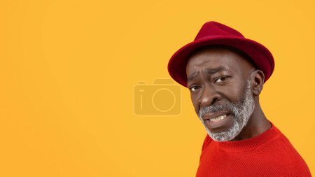 Photo for Skeptical black senior man with a questioning expression, wearing a red sweater and hat, glancing sideways with a pensive look, isolated on a bright yellow background, close up - Royalty Free Image