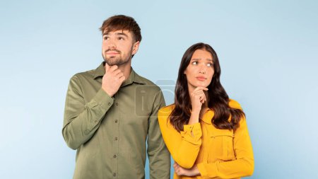 Hombre y mujer jóvenes pensativos con atuendo casual con las manos en la barbilla mirando hacia arriba, ambos perdidos en pensamiento sobre fondo azul claro