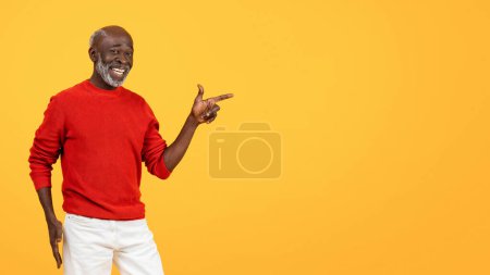 Photo for Confident senior african american man with a white beard, pointing to his right with a friendly smile, dressed in a red sweater and white pants against a bright yellow background - Royalty Free Image