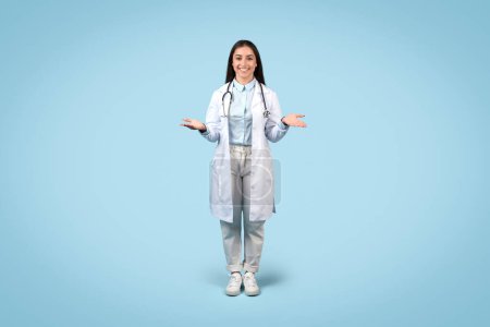 Einladende Ärztin mit freundlichem Lächeln, Geste der offenen Hände, in Labormantel und lässiger Kleidung vor beruhigendem blauen Hintergrund, Ganzkörpersicht