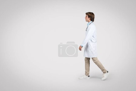 Téléchargez les photos : Vue latérale du médecin en blouse blanche, capturant le mouvement et le sentiment d'urgence en milieu clinique, fond gris, prise de vue complète - en image libre de droit