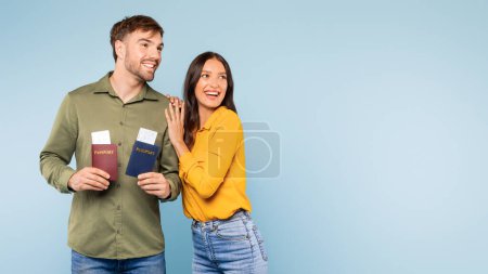 Cheerful young man and woman with passports and boarding passes in hand, looking forward to their travels, standing against calming blue background, panorama with free space