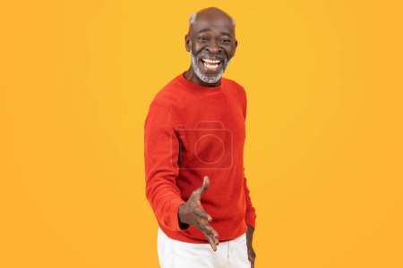 Welcoming senior african american man make handshake and smiling widely, dressed in red sweater against orange background, conveying friendliness and openness. Hello, deal