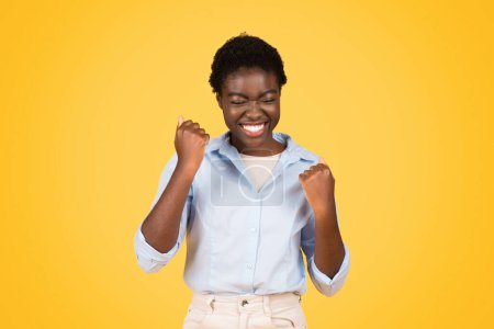 Photo for Happy young african american woman student, exuding triumph and joy, raises fists isolated on yellow background. Good news, celebrate win, success gesture, fun winner, ad and offer - Royalty Free Image