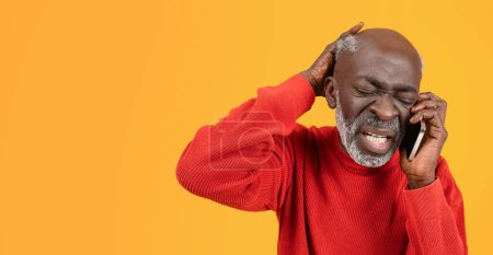 Photo for Frustrated senior black man in a red sweater and hat feeling stressed while talking on the phone, with a pained expression and hand on his head, against a yellow background - Royalty Free Image