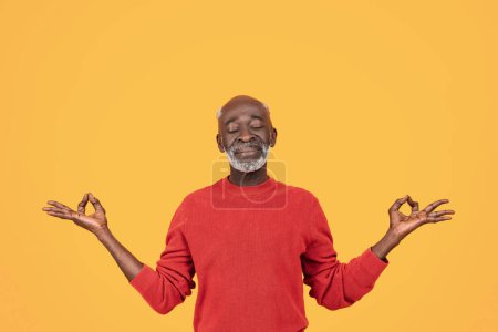 Téléchargez les photos : Homme noir senior détendu pratiquant le yoga avec une expression sereine, portant un pull rouge, effectuant un geste Gyan Mudra avec les deux mains, favorisant la tranquillité et la pleine conscience - en image libre de droit