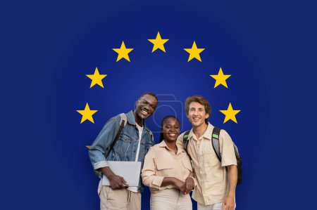 Téléchargez les photos : Trois étudiants souriants du millénaire avec des sacs à dos et un ordinateur portable debout ensemble, représentant la diversité et l'unité éducative dans un contexte de drapeau de l'Union européenne, studio - en image libre de droit