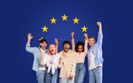 Téléchargez les photos : Exuberant groupe heureux de cinq jeunes avec les bras levés dans la victoire et la joie, célébrant la diversité devant un fond dynamique drapeau de l'Union européenne, studio, panorama - en image libre de droit