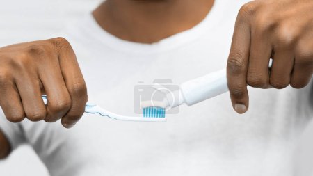 Foto de Joven hombre afro aplicando pasta de dientes en el cepillo de dientes en el baño. Concepto de pasta dental ecológica - Imagen libre de derechos