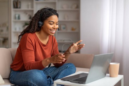 Foto de Teleconferencia. Mujer negra en auriculares haciendo videollamada en el ordenador portátil en casa, sonriendo dama afroamericana hablando y haciendo gestos en la cámara, disfrutando de la comunicación en línea, Copiar el espacio - Imagen libre de derechos