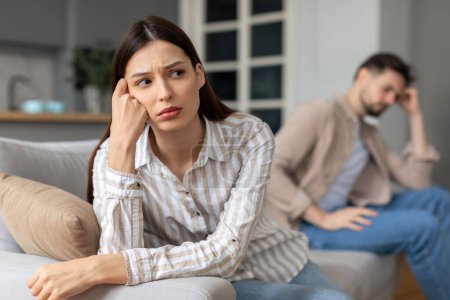Photo for Distressed young woman and man sitting separately on couch, both appearing troubled and deep in thought, highlighting relationship issues - Royalty Free Image