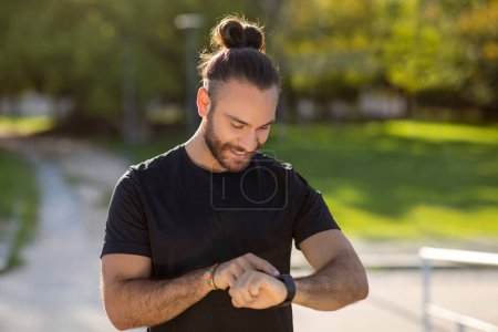 Photo for Athletic man wearing activewear monitors his workout with smartwatch outdoors. Weight loss concept highlights his dedication to fitness and exercise, with focus on wellness and health - Royalty Free Image