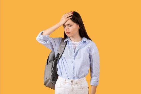 Photo for Lady with backpack touches her forehead in universal gesture of stress, forgetfulness or headache, capturing relatable moment for students everywhere - Royalty Free Image