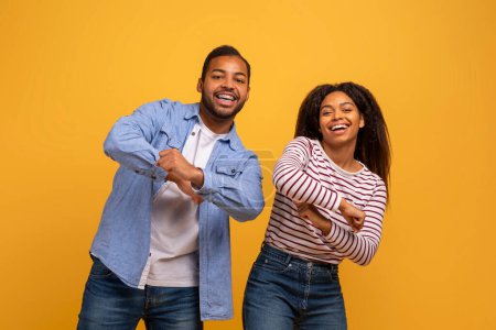 Téléchargez les photos : Jeune couple noir insouciant dansant ensemble sur fond de studio jaune, Homme et femme afro-américains positifs s'amusant et riant, Poser dans un contexte lumineux, Espace de copie - en image libre de droit