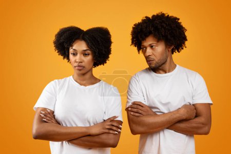 Foto de Hombre negro infeliz mirando a su esposa molesta, fondo de estudio naranja. Triste pareja afroamericana millennial cónyuges que experimentan dificultades en las relaciones, el matrimonio - Imagen libre de derechos