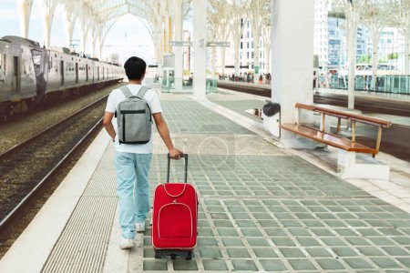Photo for Back view of young man tourist walking by train station, carrying suitcase and backpack, waiting for his train. Guy student traveling solo, full length, copy space - Royalty Free Image