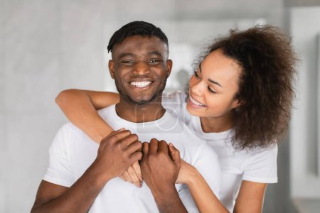 Téléchargez les photos : Affectueux couple afro-américain millénaire se tient ensemble étreignant et souriant, posant pour portrait, reflétant la joie et l'amour de leur relation dans l'intérieur de la salle de bain domestique - en image libre de droit