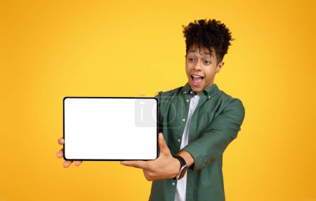 Téléchargez les photos : Incroyable jeune homme afro-américain élégant montrant tablette numérique avec écran blanc vide, étudiant recommande une belle application mobile éducative ou offre pour cours en ligne, maquette, fond jaune - en image libre de droit
