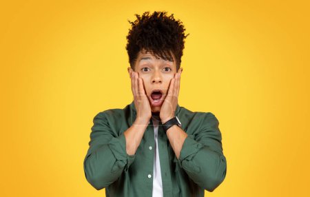 Photo for Shocked stylish millennial black guy wearing casual clothing grimacing and gesturing on yellow studio background, looking at camera with open mouth, touching his face. Emotions concept - Royalty Free Image