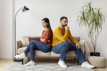 Photo for Young Couple Sitting Back To Back To Each Other On Couch At Home, Upset Millennial Man And Woman Offended After Domestic Quarrel, Suffering Family Conflicts And Problems In Relationship, Free Space - Royalty Free Image