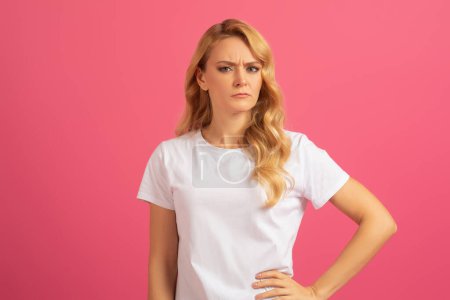Photo for Displeased blonde lady expresses serious disapproval stands with hand on hip and frowning, on pink studio background. Portrait of discontented young woman expressing negative emotion, disagreement - Royalty Free Image