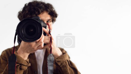 Focused male photographer peering through professional DSLR camera lens, capturing shot, with blurred background emphasizing concentration and the art of photography