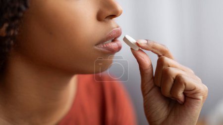Photo for Unrecognizable Young Black Woman Taking White Pill At Home, African American Female Eating Beauty Supplement Or Vitamins, Indicating Healthcare Or Wellness, Closeup Shot, Cropped Image - Royalty Free Image