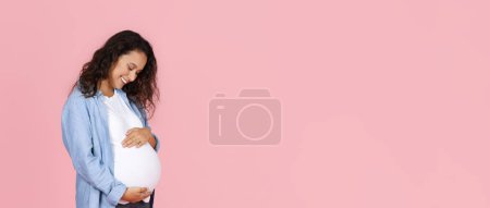 Photo for Pregnancy, motherhood. Joyful beautiful young pregnant woman embracing and looking at her big tummy, isolated on pink studio background, web-banner, panorama with copy space - Royalty Free Image