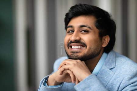 Photo for Closeup portrait of cheerful Indian entrepreneur man smiling to camera at workplace, posing with hands near chin, representing leadership and successful entrepreneurship in corporate business world - Royalty Free Image