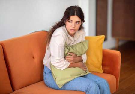 Photo for Anxious young woman sitting on sofa, hugging pillow for comfort, stressed millennial female suffering panic attack, feeling scared and upset, relaxing in living room interior at home, copy space - Royalty Free Image