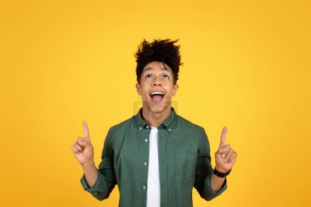 Photo for Happy stylish handsome young black guy pointing up at copy space for advertisement or text above his head, isolated on yellow studio background. Great offer, deal - Royalty Free Image