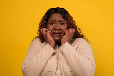 Téléchargez les photos : Effrayée femme afro-américaine en surpoids millénaire grimaçant et touchant son visage, isolée sur fond de studio jaune, regardant quelque chose d'effrayant - en image libre de droit