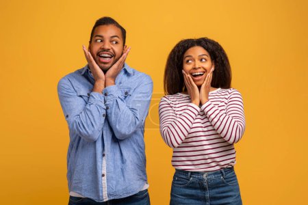 Photo for Amazed young black couple with hands on cheeks showing surprised expressions, cheerful african american man and woman standing wide-eyed and excited against yellow studio background, copy space - Royalty Free Image