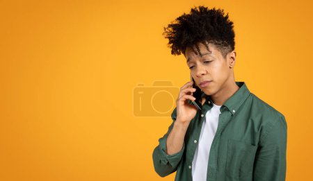 Foto de Triste hombre afroamericano millennial con estilo tienen conversación telefónica sobre fondo de estudio amarillo, panorama con espacio de copia. Joven hombre negro escuchar malas noticias - Imagen libre de derechos