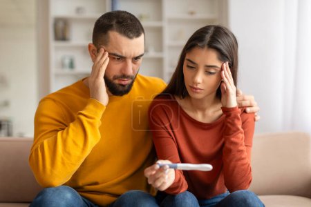 Photo for Portrait Of Upset Young Spouses Looking At Negative Pregnancy Test, Suffering Infertility Problems, Depressed Millennial Couple Sitting Together On Couch At Home, Having Health Issues, Closeup Shot - Royalty Free Image