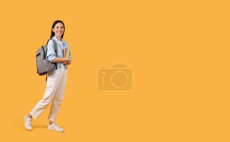 Photo for Smiling student lady walks confidently, holding notebooks and wearing backpack, embodying optimism and preparedness for academic challenges, free space - Royalty Free Image