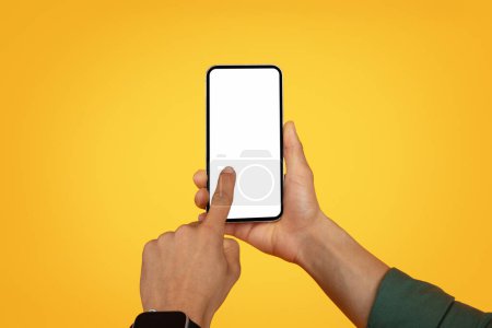 Téléchargez les photos : Mains de l'homme afro-américain tenant smartphone avec écran blanc blanc espace de copie de maquette. Recadré de noir utilisateur toucher téléphone portable avec affichage vide, fond jaune - en image libre de droit