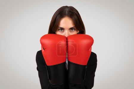 Photo for Determined caucasian businesswoman with a focused gaze wearing boxing gloves, symbolizing empowerment, challenge, competition in the corporate world, and readiness to face obstacles - Royalty Free Image