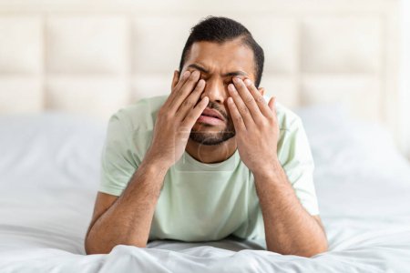 Photo for Upset broken african american young man wearing pajamas lying on bed at home in the morning, touching eyes with palms, crying, suffer from midlife crisis, experience difficulties in life, copy space - Royalty Free Image