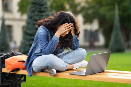 Téléchargez les photos : Désespérée et en détresse, une jeune étudiante indienne étudiant sur ordinateur portable sur le campus du collège, faisant face à des défis avec l'apprentissage numérique et rencontrant des problèmes avec son tutoriel en ligne. - en image libre de droit