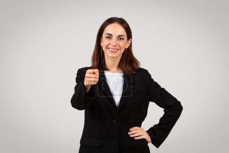 Photo for Professional, confident caucasian young woman in business attire pointing directly at camera with a friendly smile, standing against a neutral background, studio. Motivation - Royalty Free Image