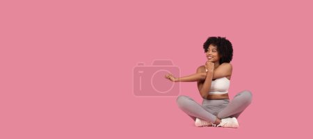 Téléchargez les photos : Femme afro-américaine en tenue de sport blanche effectuant un exercice d'étirement du bras assis sur fond rose, panorama avec espace libre, bannière - en image libre de droit