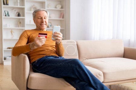 Photo for Happy senior grey-haired man using smartphone and credit card at home, sitting on couch, order food online, using delivery mobile application, banking or shopping on Internet, copy space - Royalty Free Image