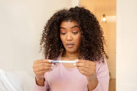 Foto de Mujer negra impactada revisando la prueba de embarazo en casa, sintiéndose sorprendida con el resultado. Joven mujer afroamericana que tiene problemas, frente a la maternidad no deseada, no está listo para la maternidad, primer plano - Imagen libre de derechos