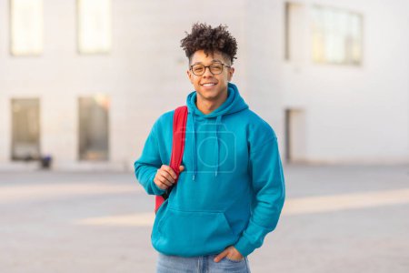 Photo for Portrait of successful brazilian student guy wearing eyeglasses standing with backpack outdoor on backdrop of modern college building in urban area, smiling to camera. Free space - Royalty Free Image