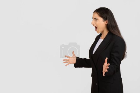 Photo for Professional young woman in black suit angrily gesturing and shouting, speaking with an expressive face, isolated on light grey background, copy space - Royalty Free Image