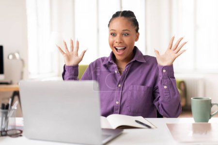 Photo for Surprised and joyful lady student raises her hands in excitement while studying and looking at her laptop, sitting in well-lit home environment, receiving test results - Royalty Free Image